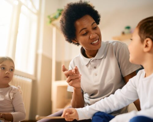 Black female teacher talking to kids during music class at preschool. African American teacher communicating with children while playing music together at kindergarten.